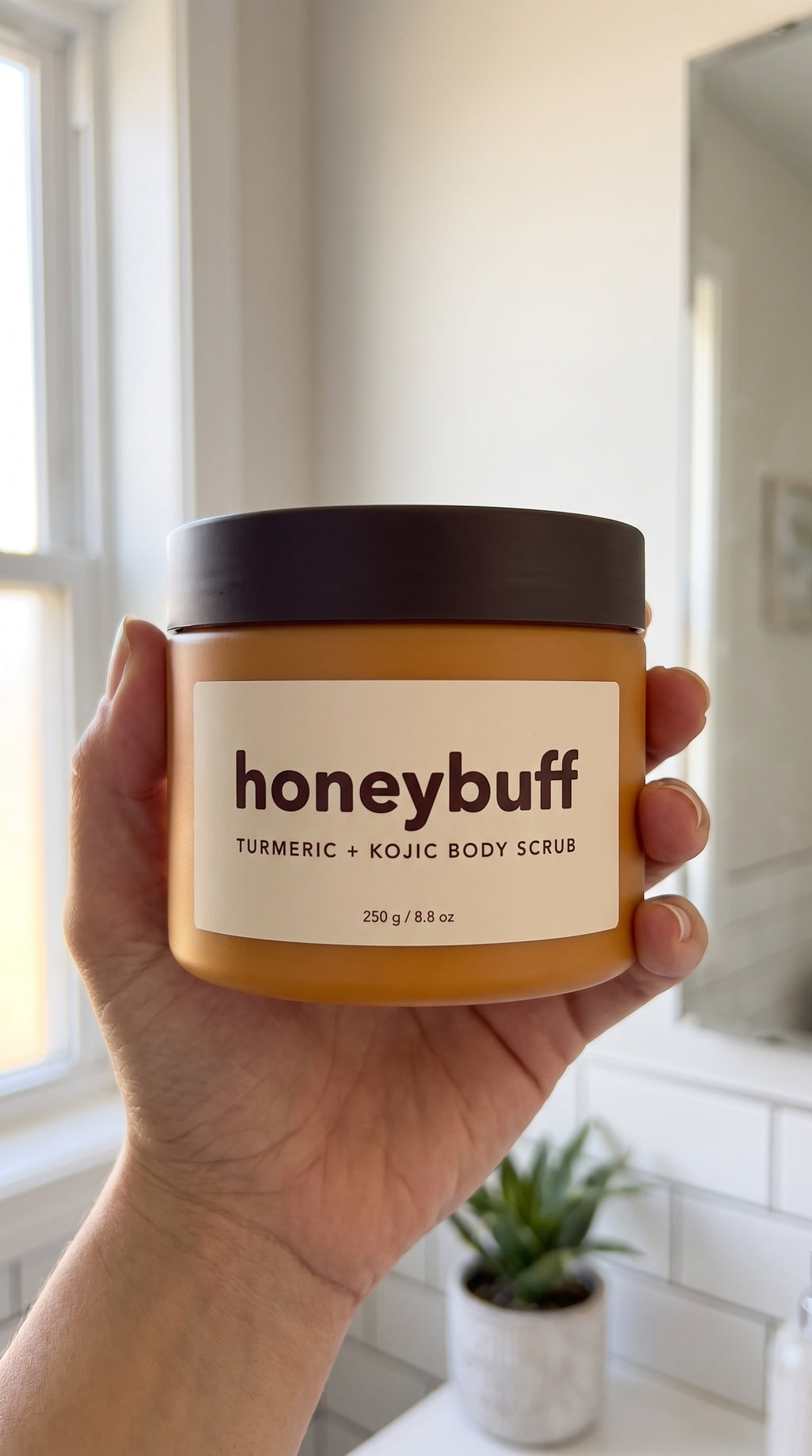 A hand holding the Honeybuff jar in the shower